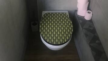 Un baño pequeño y moderno con inodoro, soporte para papel higiénico y un interruptor de luz en la pared.
