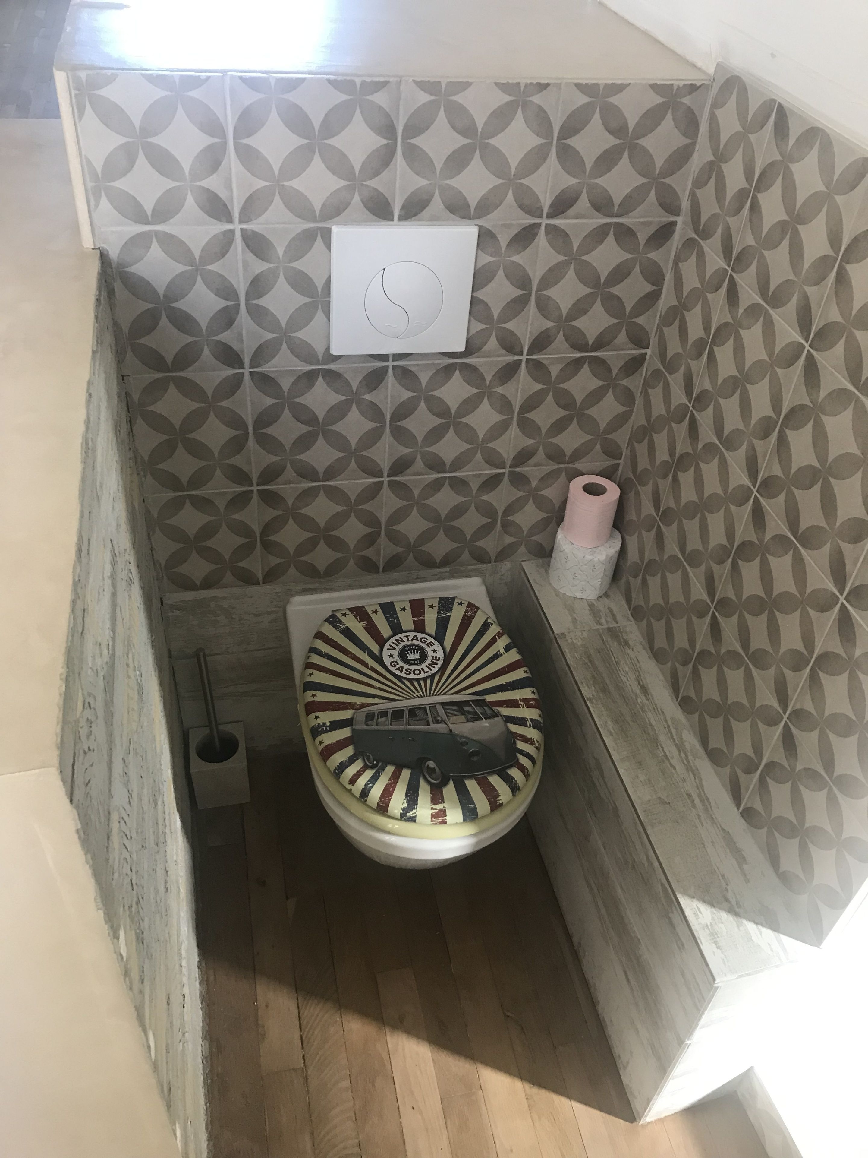 Ein Badezimmer mit einer Wand aus gemusterten Fliesen, einer Toilette im Vintage-Stil und einem Toilettenpapierhalter.