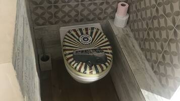 Ein Badezimmer mit einer Wand aus gemusterten Fliesen, einer Toilette im Vintage-Stil und einem Toilettenpapierhalter.