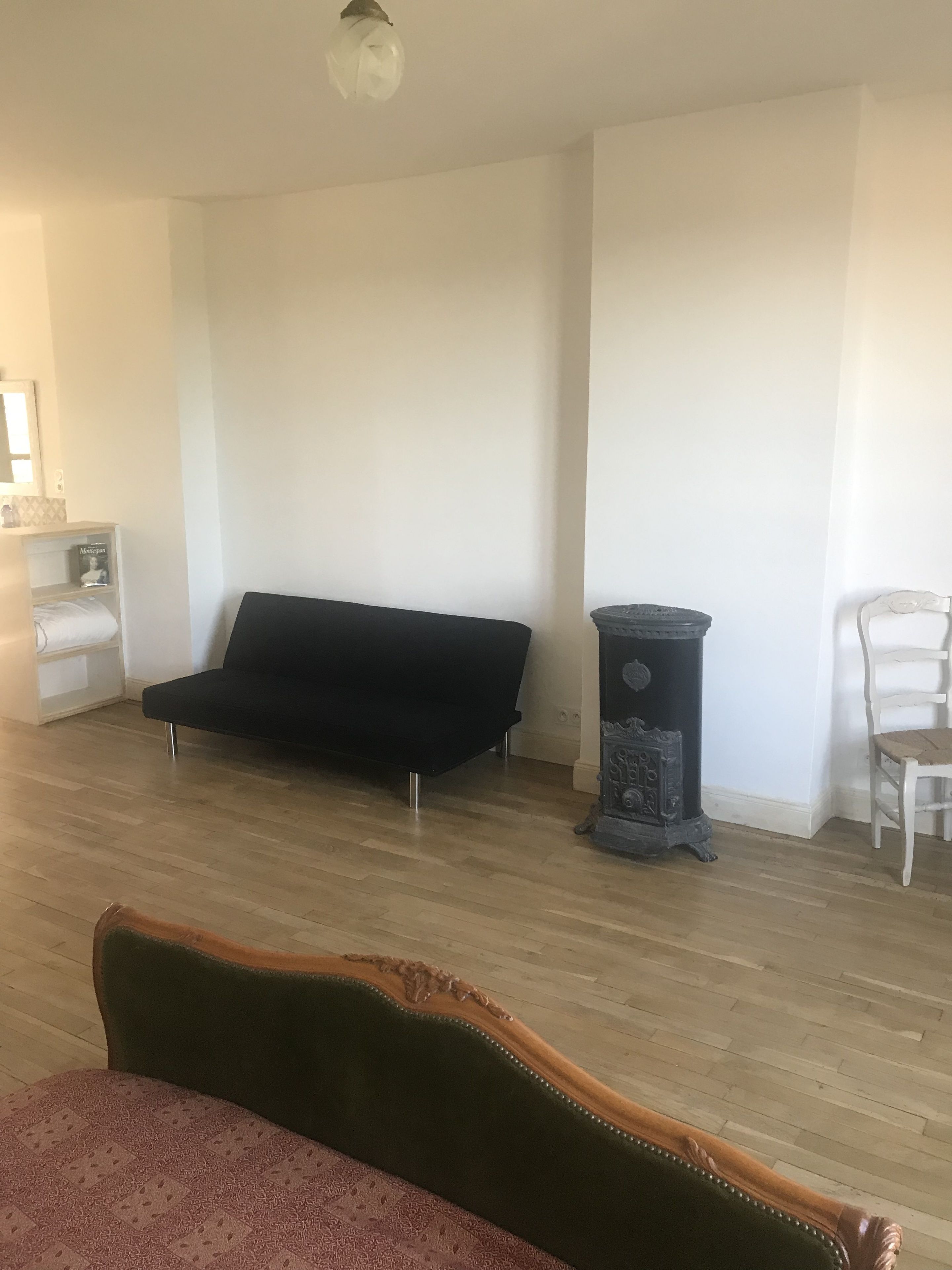 Ett rum med en svart soffa, en vit stol, ett litet bord och en dekorativ kamin.