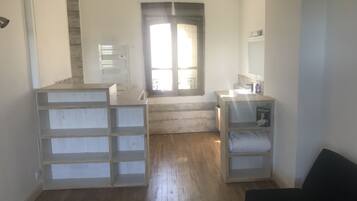 A room with a wooden floor, a black chair, a white shelf unit, and a window with curtains.