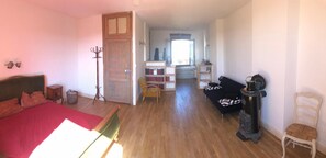 A bedroom with a bed, a wooden door, a bookshelf, a black sofa, and a white chair. - Librairie Abelard (Montolieu)