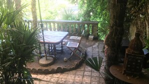 A patio area with a table and chairs, surrounded by lush greenery and a stone pathway. - Librairie Abelard (Montolieu)
