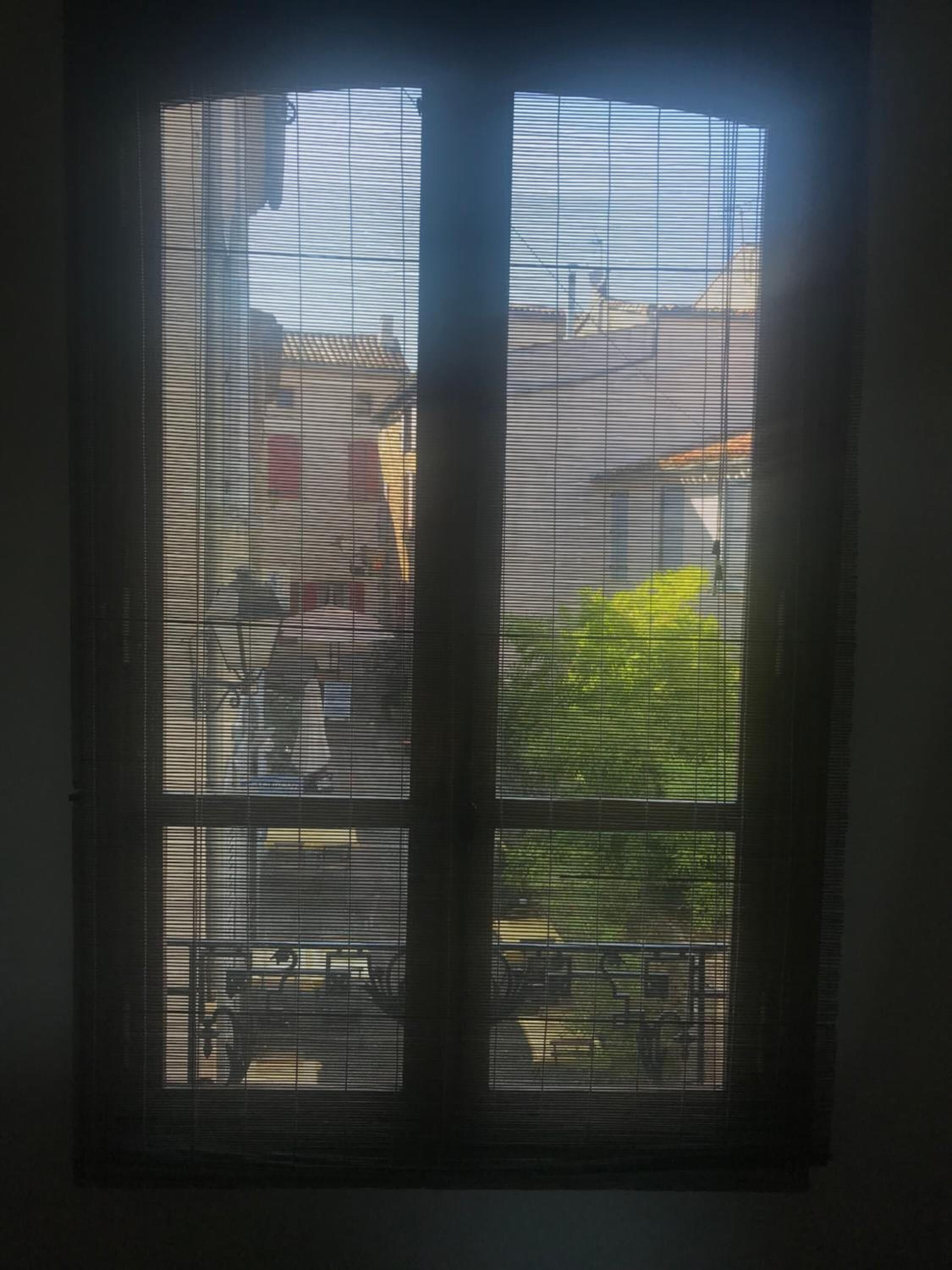Una ventana con persianas horizontales, vista exterior de edificios y cielo despejado.
