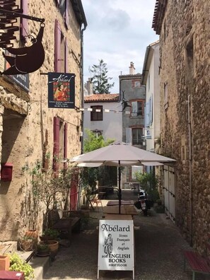 A narrow street with buildings on either side, a sign for 'Abélard' bookstore, outdoor seating, and a parked motorcycle. - Librairie Abelard (Montolieu)