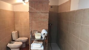 A bathroom with a toilet, a shower, and a shelf with towels. - Hotel Patri (Huescar)