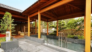 A covered outdoor area with a stone-tiled floor, a small water feature, and wooden structures. - Yurakujo (Tomisato)