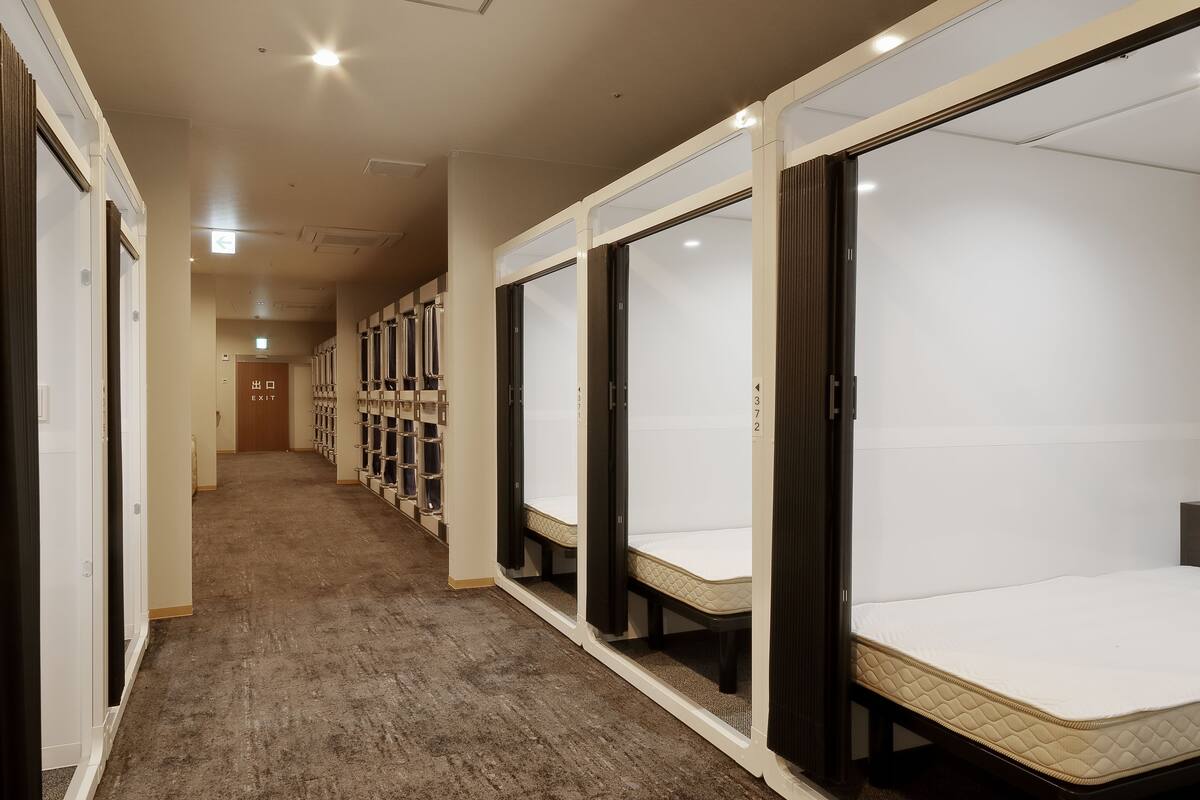 A hotel corridor with individual rooms featuring beds, a carpeted floor, and a door marked "EXIT".