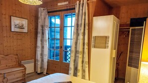 Ein Zimmer mit Holzboden, einem Bett, einem Schminktisch, einem Kleiderschrank und einem Fenster mit Vorhängen.