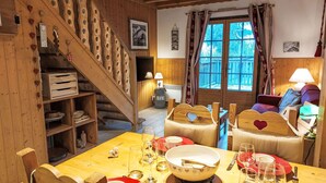 Ein gemütliches Holzinnenleben mit einem Esstisch für vier Personen, einer Treppe mit herzförmigen Ausschnitten und einem Fenster mit Vorhängen.