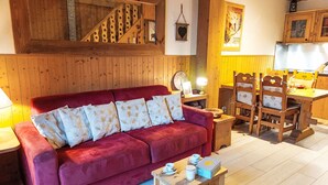 Ein gemütliches Wohnzimmer mit einem roten Sofa, Holzwänden, einem Essbereich mit Holzsesseln und einem kleinen Tisch mit einer Lampe.