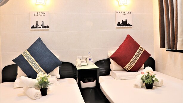 A hotel room with two beds, each with a pillow and a small potted plant. There are two signs on the wall, one labeled "Lisbon Portugal" and the other "Marseille France". - The One Inn (Kowloon)