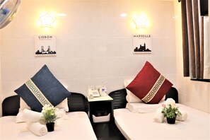 Quarto de hotel com duas camas, cada uma com um travesseiro e um pequeno vaso de planta. Existem dois sinais na parede, um com a inscrição "Lisboa Portugal" e outro com "Marselha França".