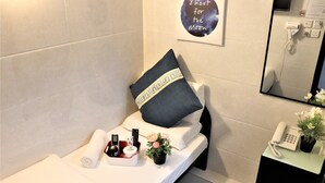 A neatly made bed with a pillow, a small bedside table with a phone, a remote control, and a vase with flowers. - The One Inn (Kowloon)