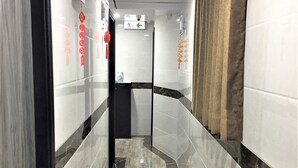A corridor with marble flooring, white walls, and red decorations. - The One Inn (Kowloon)