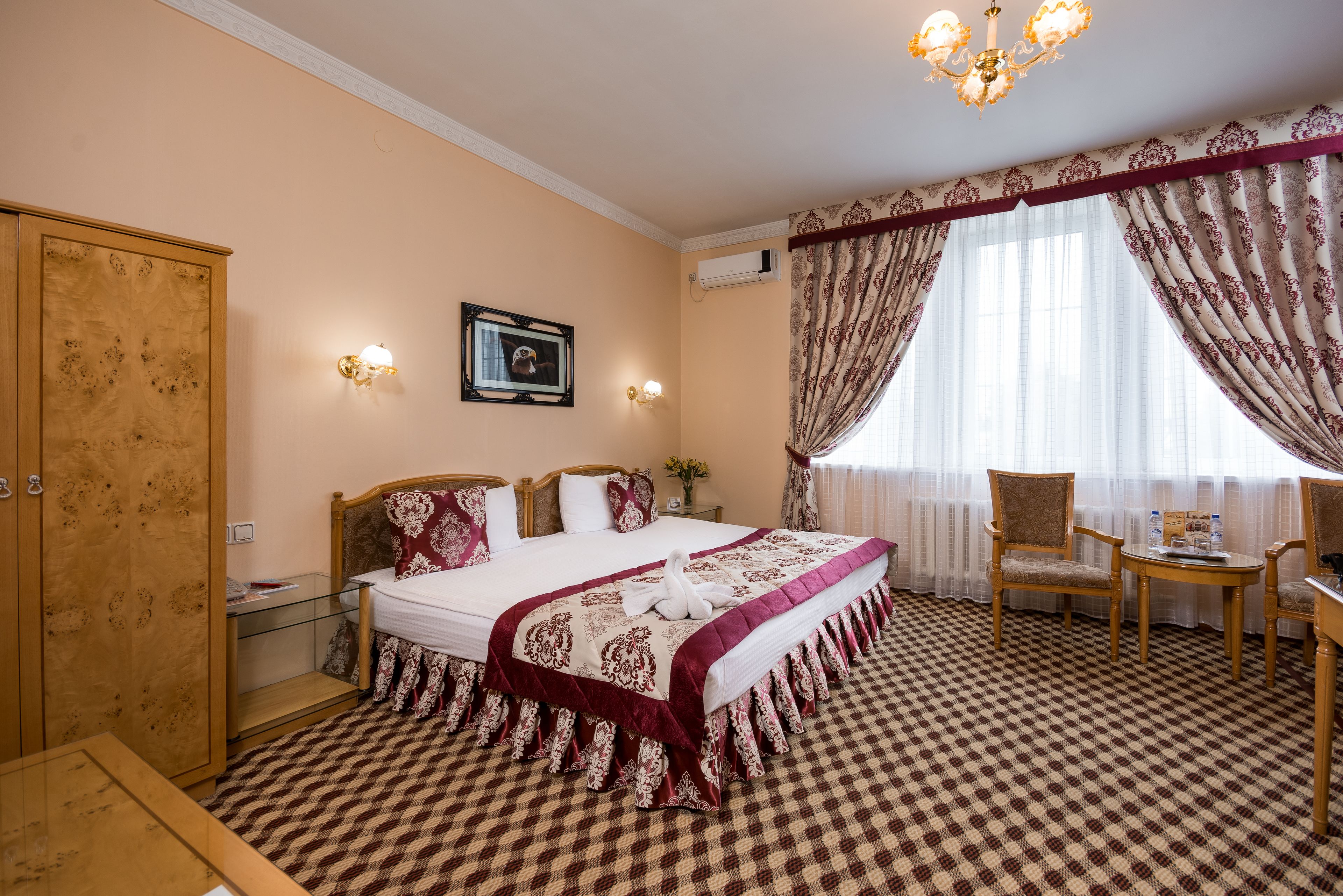 A hotel room with a large bed, a wooden wardrobe, a glass table, and a chair.