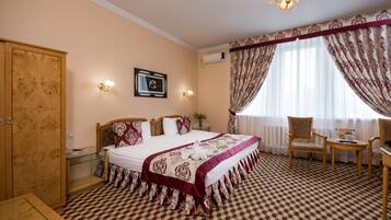 A hotel room with a large bed, a wooden wardrobe, a glass table, and a chair.