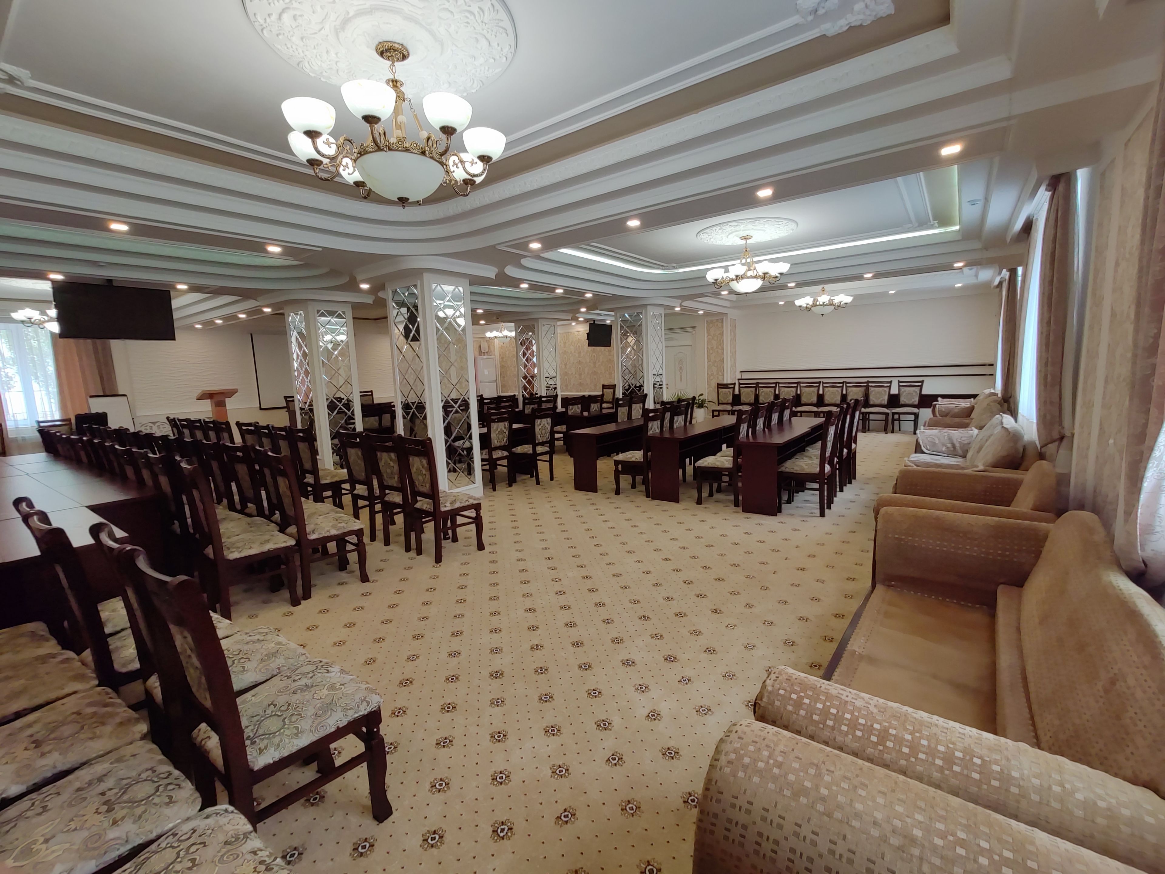 A spacious conference room with high ceilings, ornate chandeliers, and a patterned carpet.