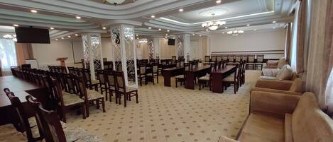 Una amplia sala de conferencias con techos altos, candelabros ornamentados y una alfombra estampada.