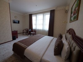 A hotel room with a bed, a desk with two chairs, a television, and a window with curtains.