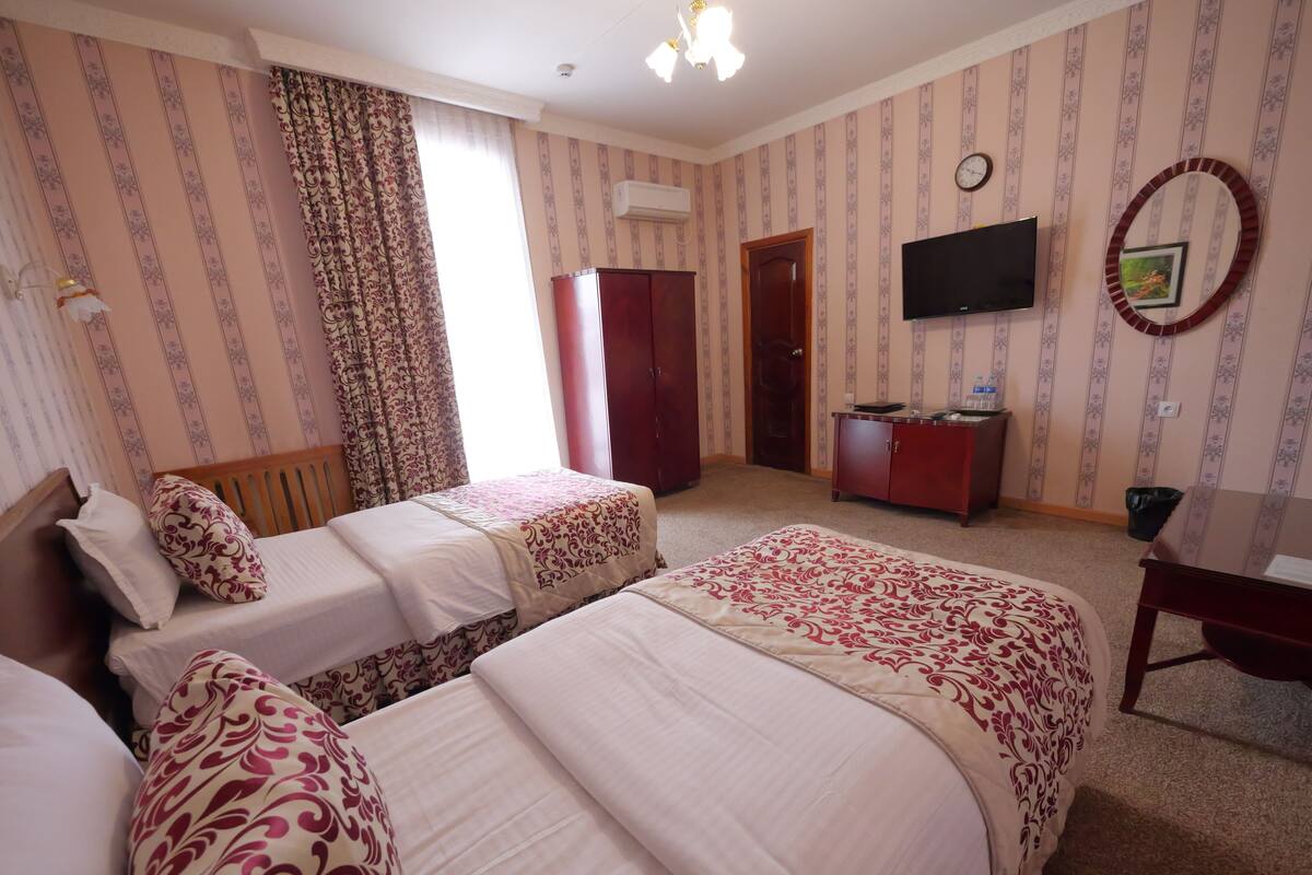 Een hotelkamer met twee bedden, een kledingkast, een televisie en een spiegel.