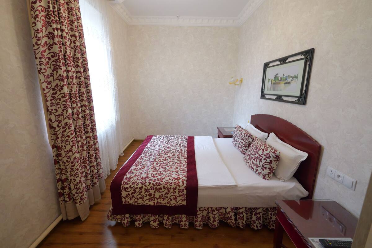 Een opgemaakt bed met een bedsprei en kussens, een nachtkastje met een afstandsbediening, en een lijstje met een foto aan de muur.