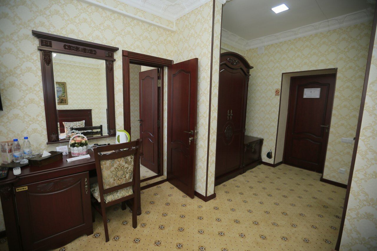 Ein Hotelzimmer mit Schreibtisch aus Holz, einem Sessel, einem großen Spiegel und einem Kleiderschrank.