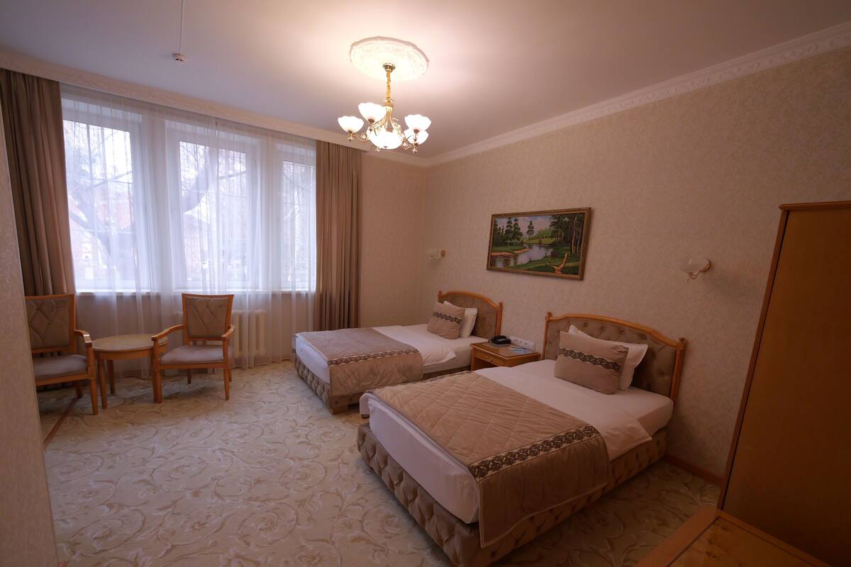 Een hotelkamer met twee bedden, een stoel, een bureau en een schilderij aan de muur.
