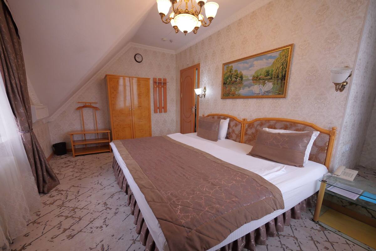 Een slaapkamer met een groot bed, een houten kledingkast en een schilderij aan de muur.