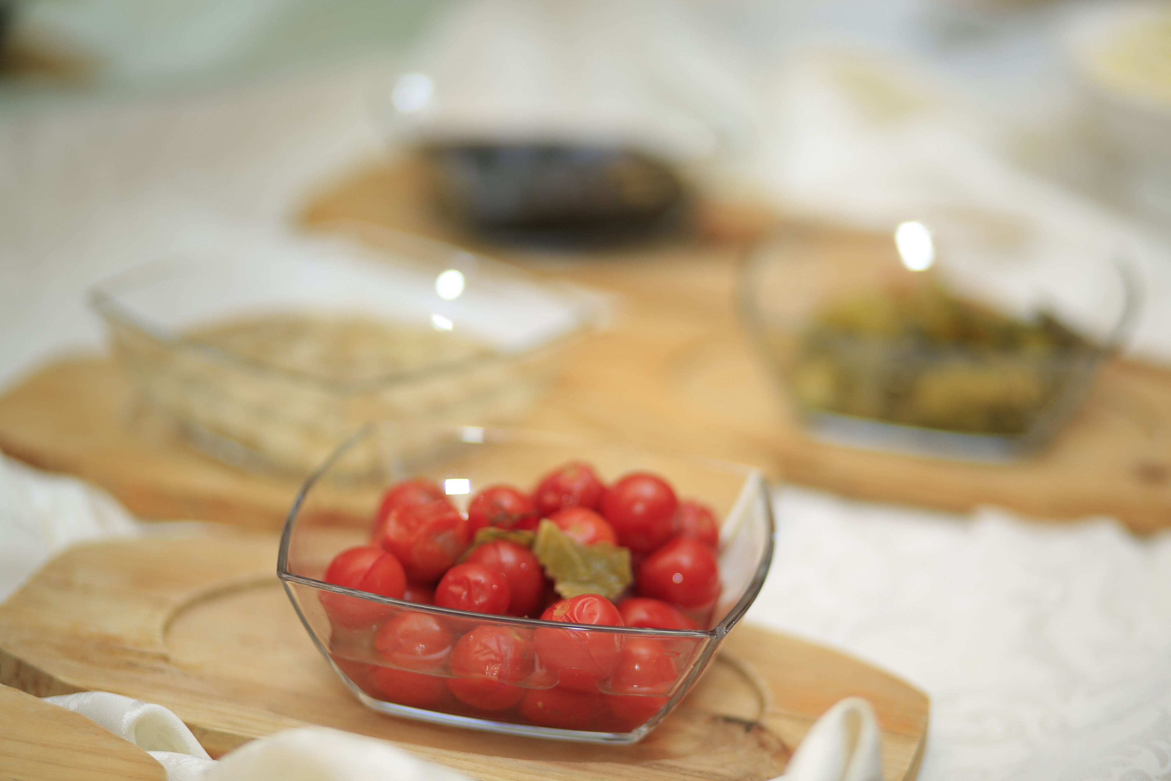 Un cuenco de vidrio transparente lleno de tomates rojos sobre una tabla de madera.