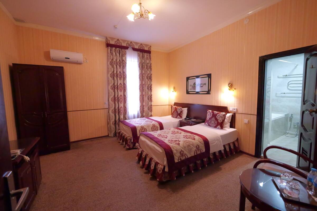 Een hotelkamer met twee bedden, een bureau, een stoel, een douchecel van glas en een kledingkast.