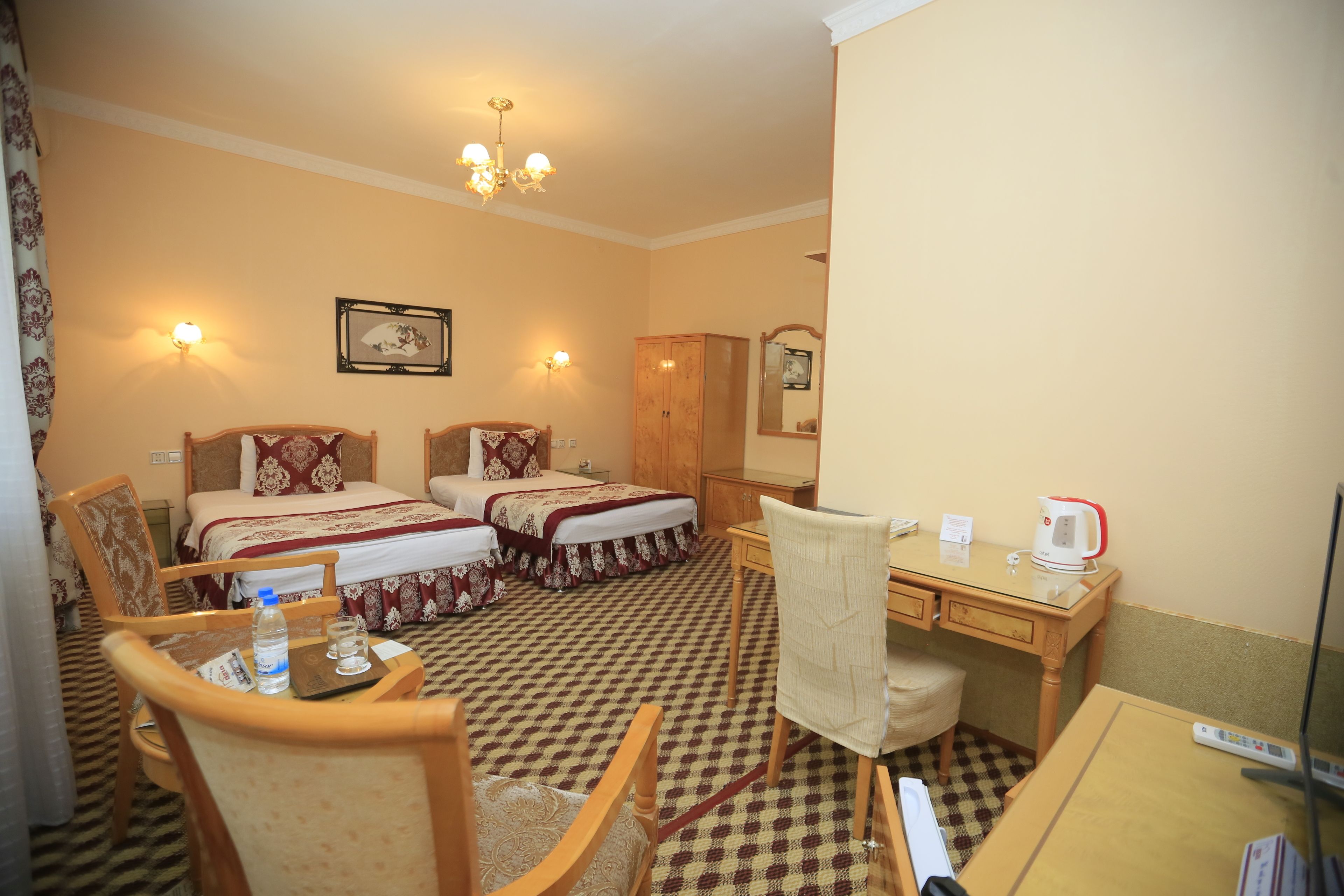 A hotel room with two beds, a desk, a chair, a wardrobe, and a mirror.