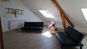 A loft-style room with a sloped ceiling, a black sofa, a wooden bench, and a small table with a vase of flowers. - Gite de la Draye (Crots)