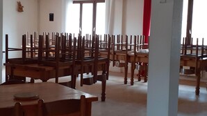 A room with multiple wooden tables and chairs arranged in rows, a white pillar, and a red curtain. - Gite de la Draye (Crots)