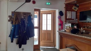 A room with a wooden door, a coat rack with jackets, a bar area with glasses and bottles, and a television on the wall. - Gite de la Draye (Crots)