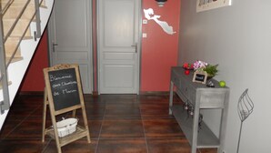 Een gang met een trap, een prikbord, een console tafel met decoratieve objecten, en een muur met een geschilderde silhouet.