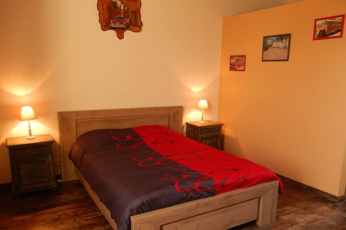 Een slaapkamer met een houten bed, twee bedlampen, een rood-zwarte dekbedovertrek en een houten vloer.
