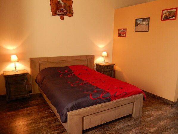 A bedroom with a wooden bed, two bedside lamps, a red and black bedspread, and a wooden floor. - Les Chambres de Manou (Moreilles)