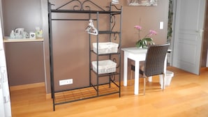 Een kamer met een metalen rek met manden, een witte tafel met een stoel, en een Boeddha-schilderij aan de muur.