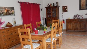 Een eethoek met een houten tafel en stoelen, een rood gordijn en een kast met glazen deuren.