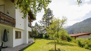Una casa moderna amb un balcó, un jardí petit i un paisatge de muntanya al fons.