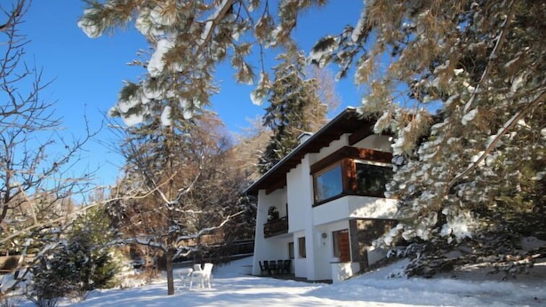 Una xalet de dues plantes amb un teulat cobert de neu i un cel blau clar.