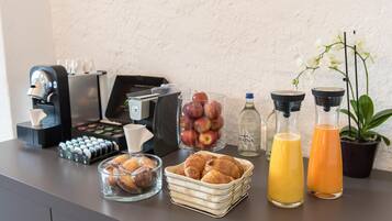 A breakfast buffet with coffee machines, pastries, fruits, and juice dispensers.