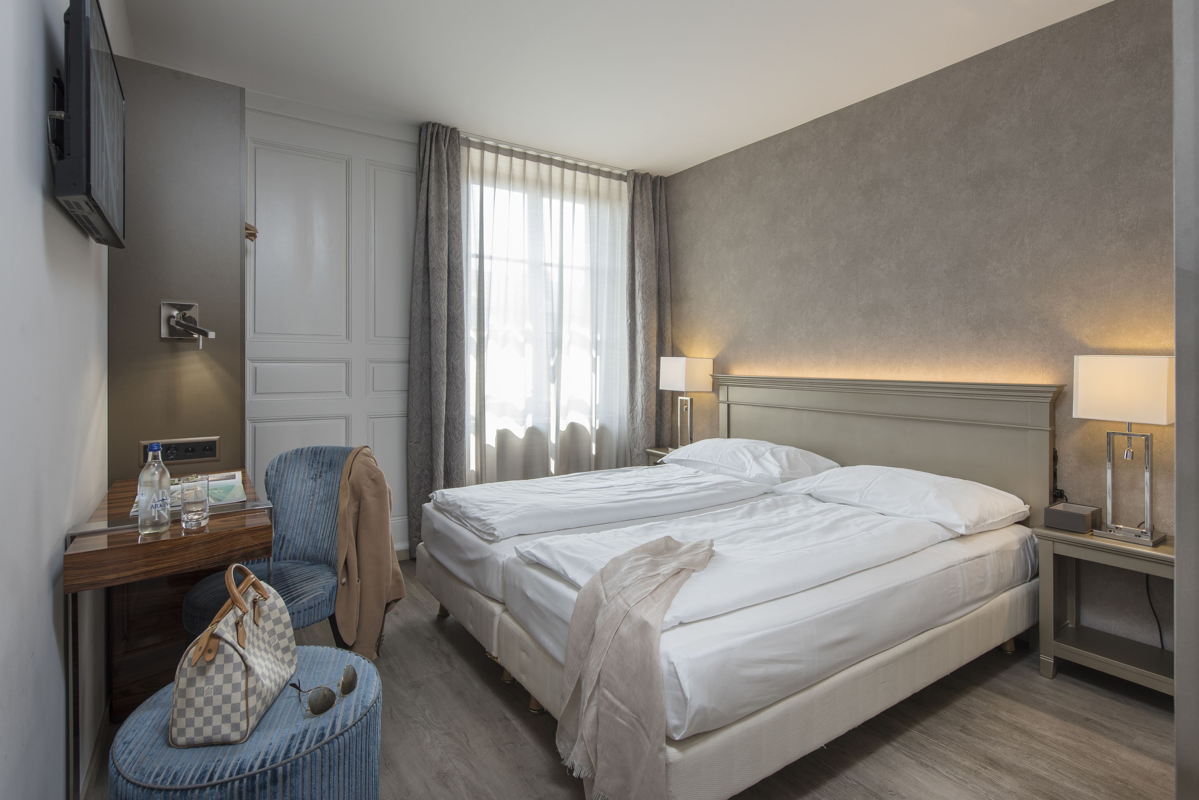 A hotel room with a bed, a desk with a chair, a TV, and a lamp.