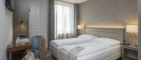 A hotel room with a bed, a desk with a chair, a TV, and a lamp.