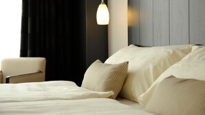 A neatly made bed with a white bedspread and pillows, a hanging pendant light, a chair, and a dark wooden headboard. - Hôtel du Théâtre (Yverdon-les-Bains)