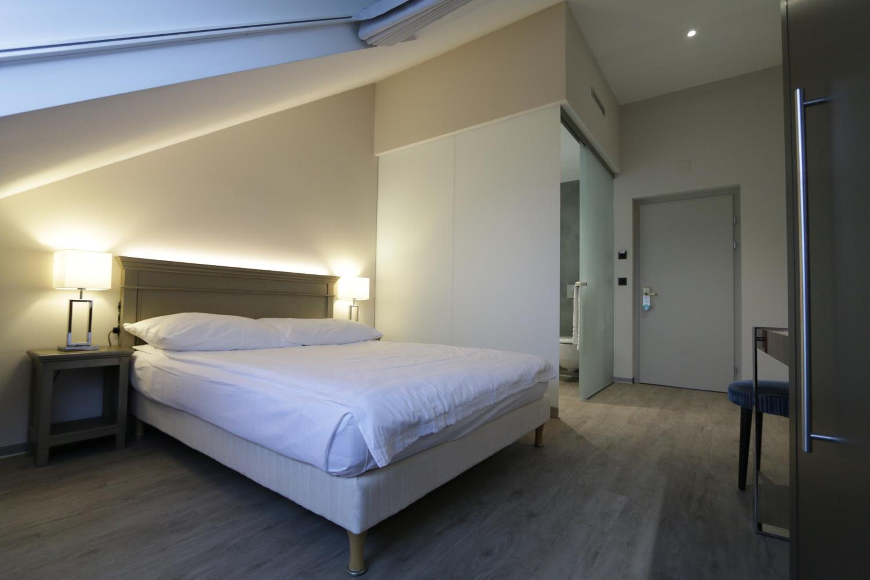 A modern bedroom with a large bed, bedside lamps, a wardrobe, and a door.