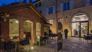 An outdoor patio area with stone flooring, metal chairs, and tables. There are potted plants and a decorative metal sculpture. - Hôtel du Théâtre (Yverdon-les-Bains)