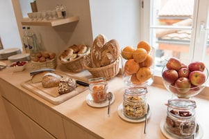 Un bufé de desayuno con pan, frutas y recipientes con mermeladas y otros acompañamientos.