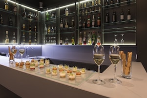 Zona de bar con botellas y vasos ordenados, y una bandeja de vidrio con aperitivos.